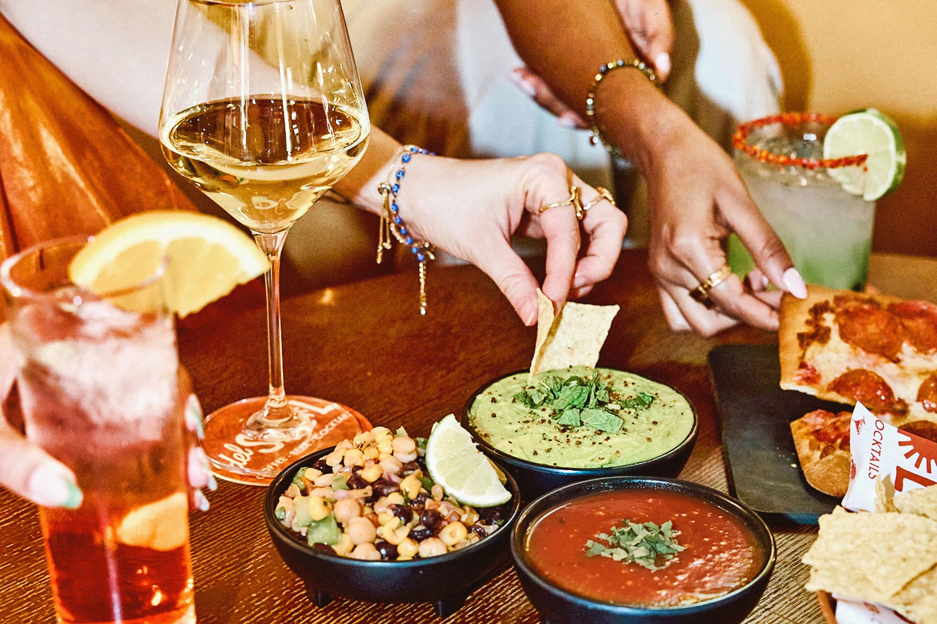 Una mesa con diversos platos, bebidas y una copa de vino blanco.