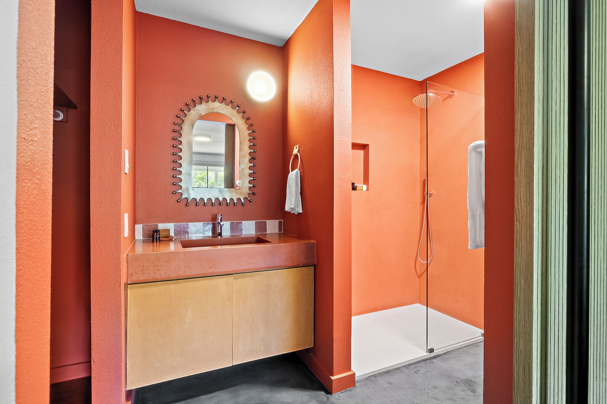 Une salle de bain avec un mur rouge, un lavabo avec un miroir et une douche.