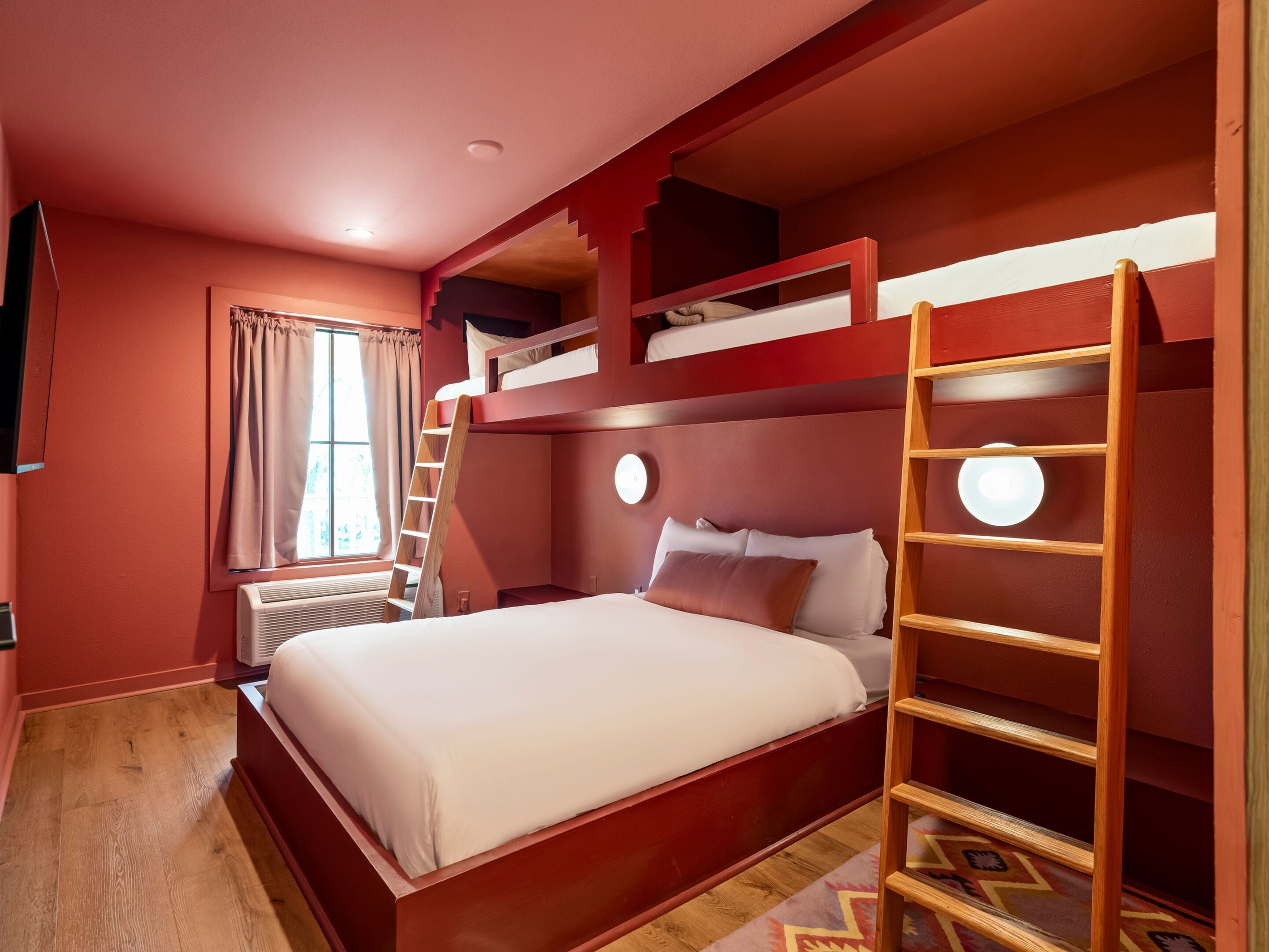 Habitación con literas, una escalera, una ventana con cortinas y un calentador fijado a la pared.