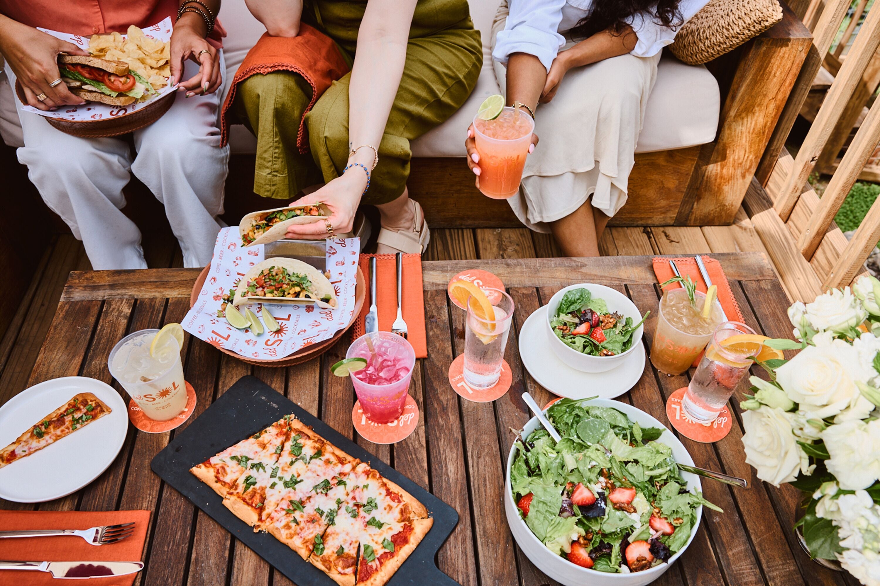 A wooden table with food, drinks, and a pizza.