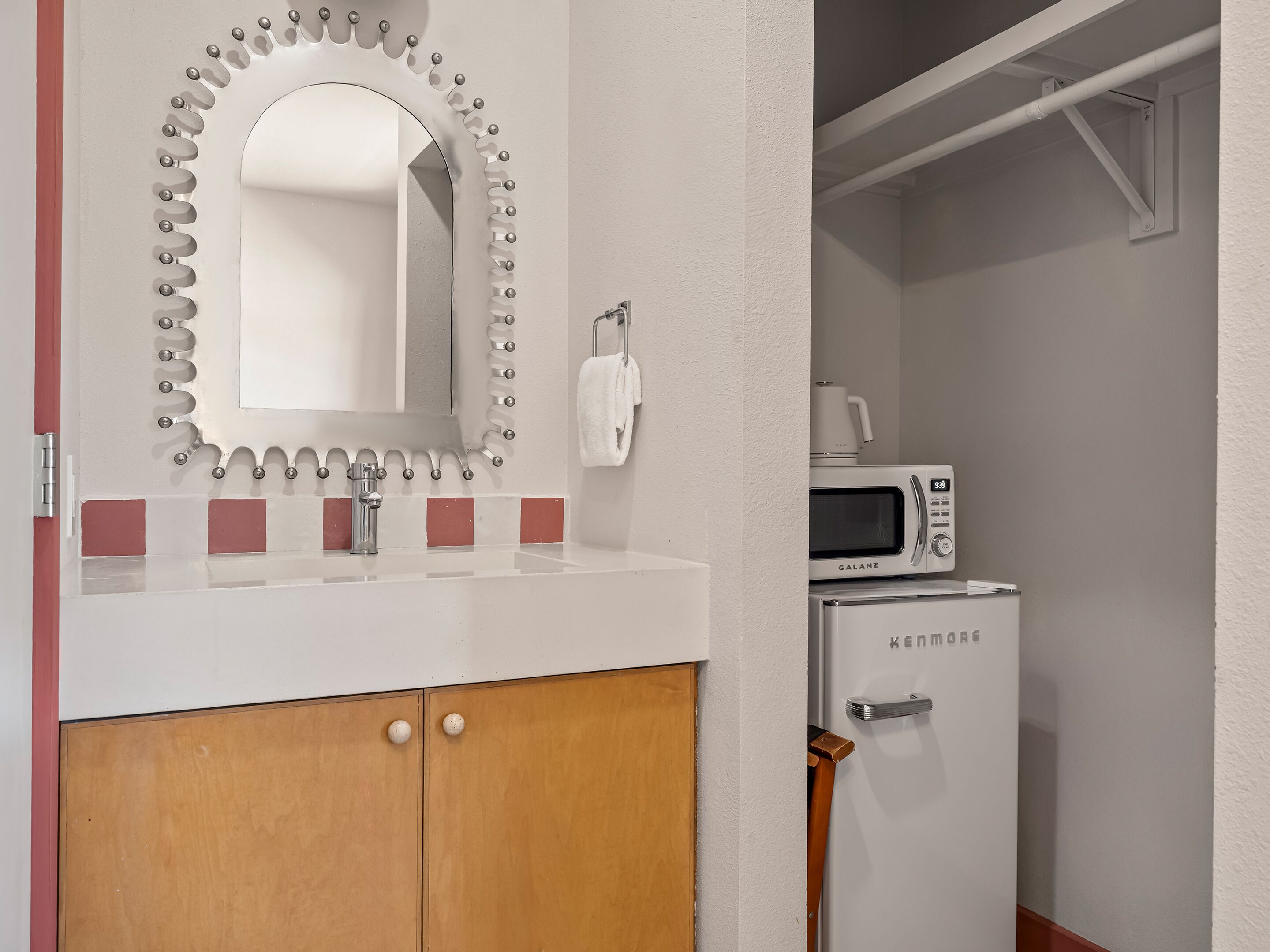 Une salle de bain comprenant un meuble-lavabo, un miroir avec des éclairages décoratifs, un évier, un placard, un four à micro-ondes et un petit réfrigérateur.