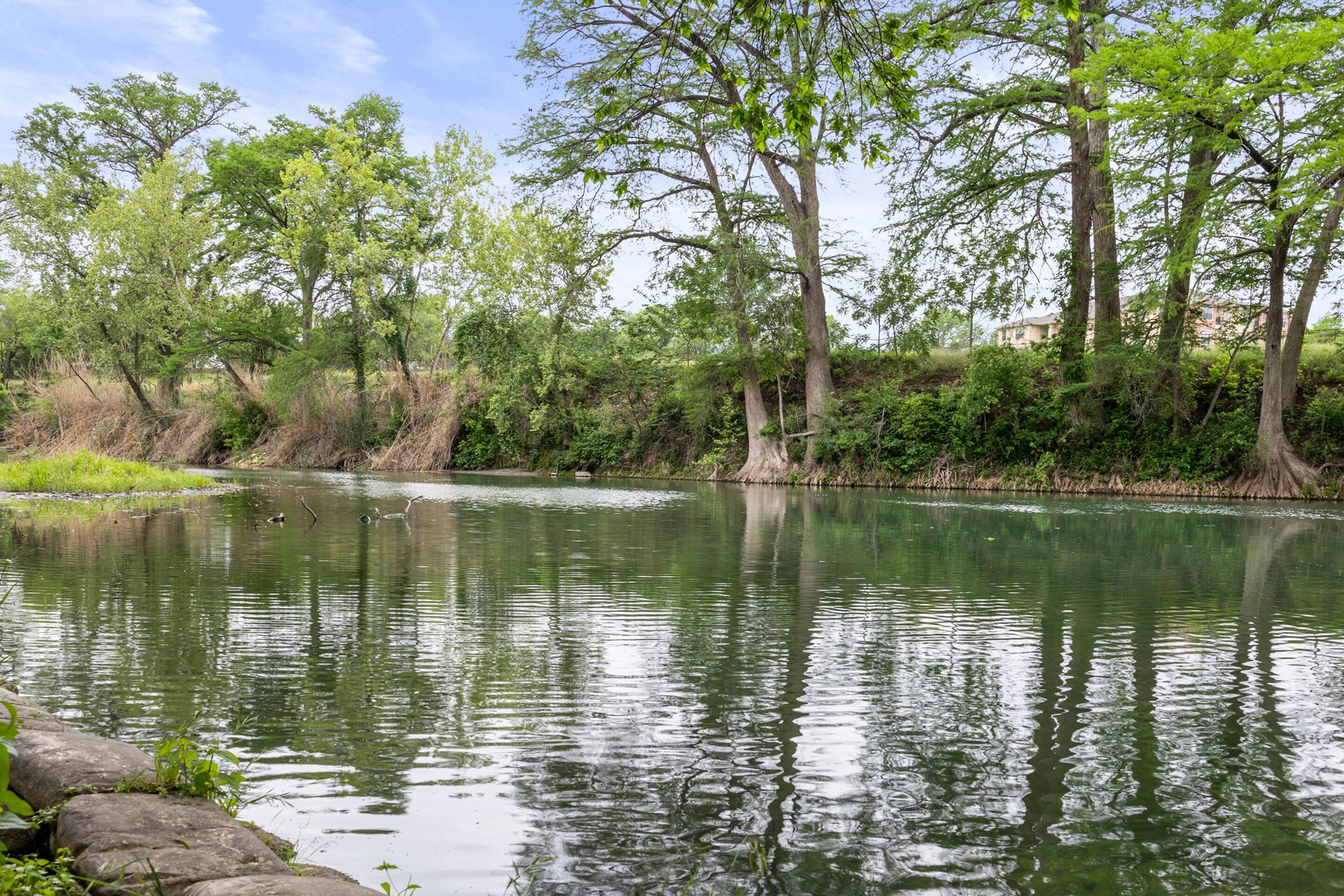 A calm river with trees and a stone wall.