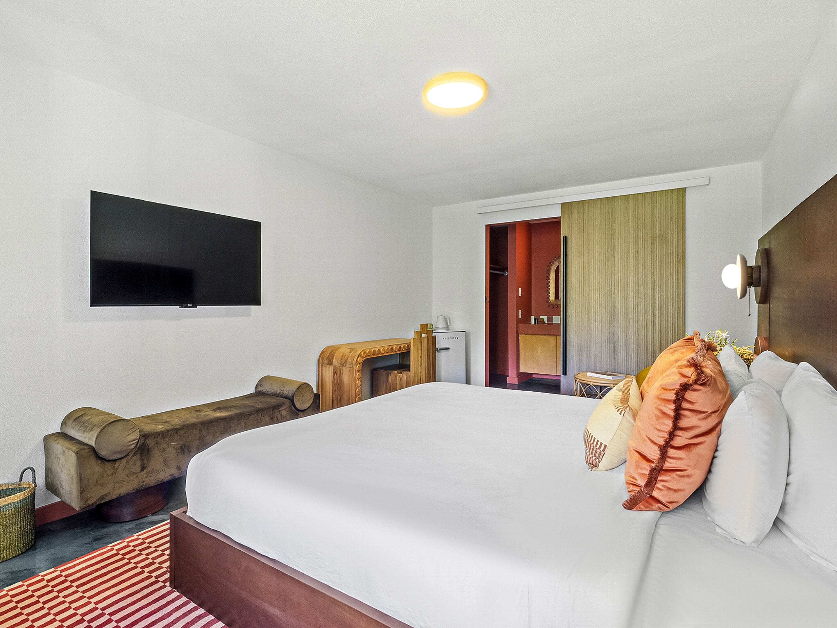 Una habitación de hotel con una cama, televisión, un banco de madera y una mesita con una taza.