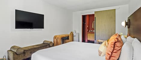 Una habitación de hotel con una cama, televisión, un banco de madera y una mesita con una taza.