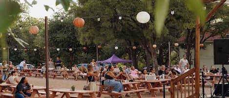 Un área de estar al aire libre con mesas de picnic de madera y luces colgantes.