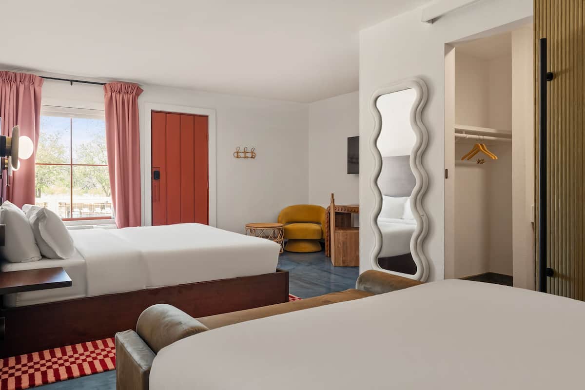 A hotel room with two beds, a mirror, a chair, a wardrobe, and a window with curtains.