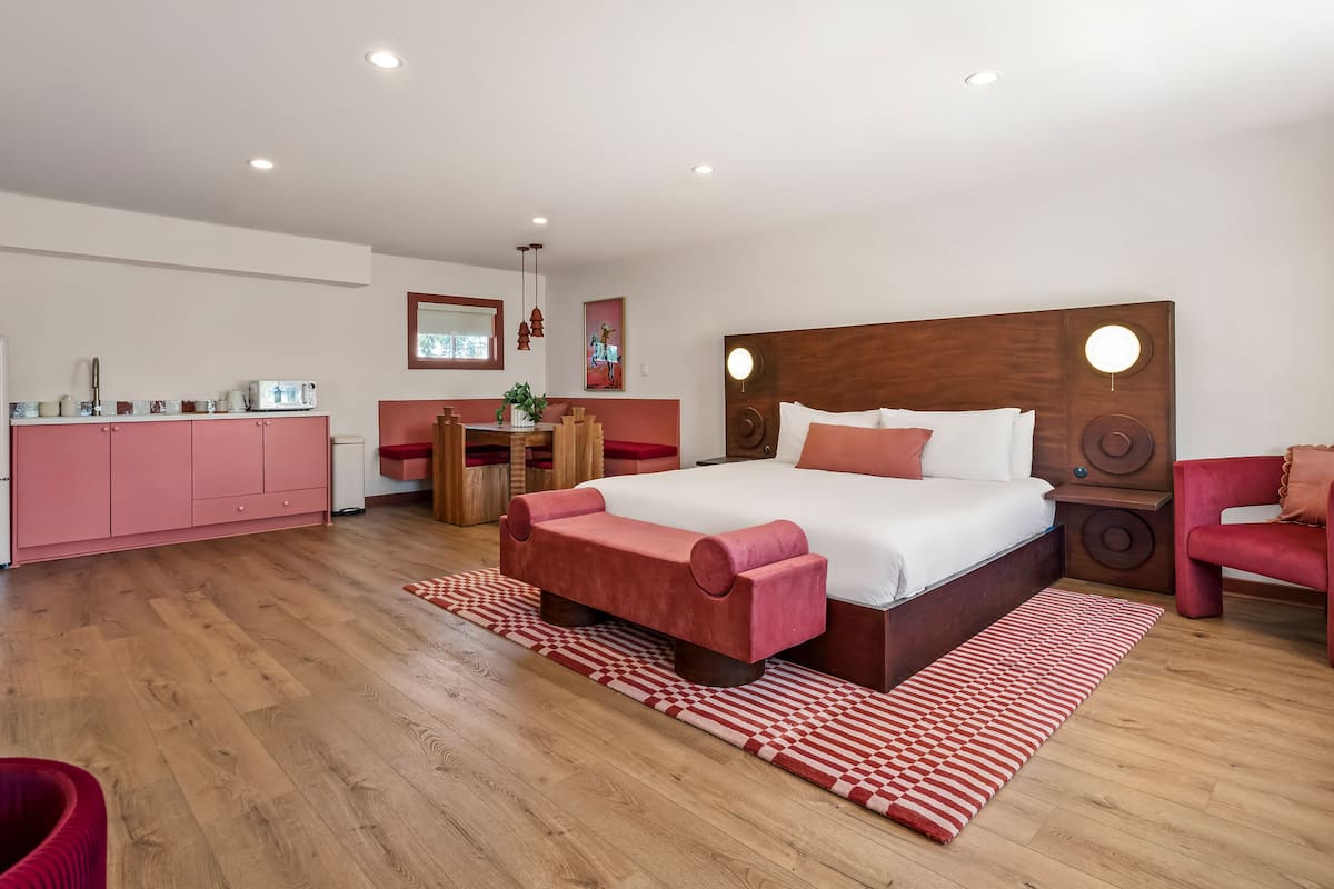 A bedroom with a large bed, a wooden headboard, a red sofa, a dining area, and a pink cabinet.