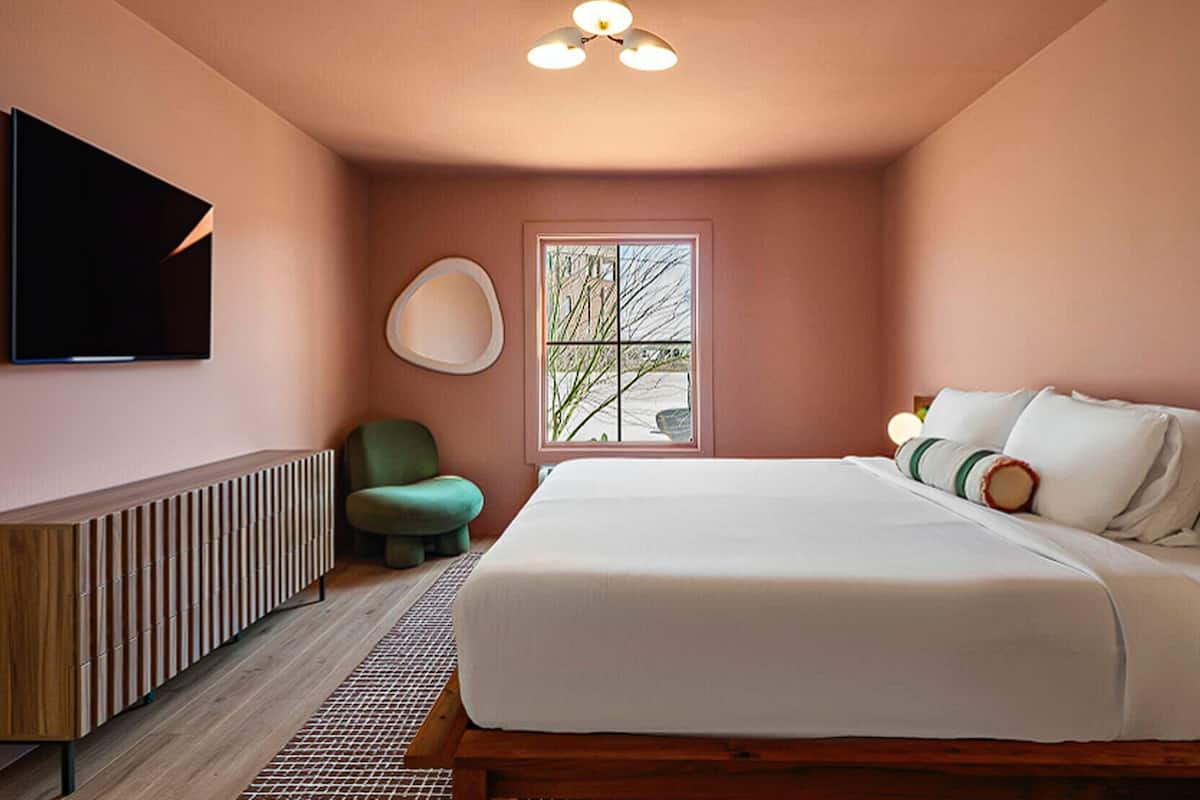 A bedroom with a bed, a TV, a radiator, a window, and a ceiling light.
