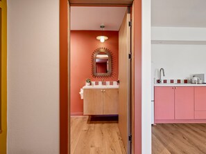 A hallway leading to a bathroom with a wooden cabinet, a mirror with a unique border, and a sink with a faucet. - Hacienda del Rio (New Braunfels)