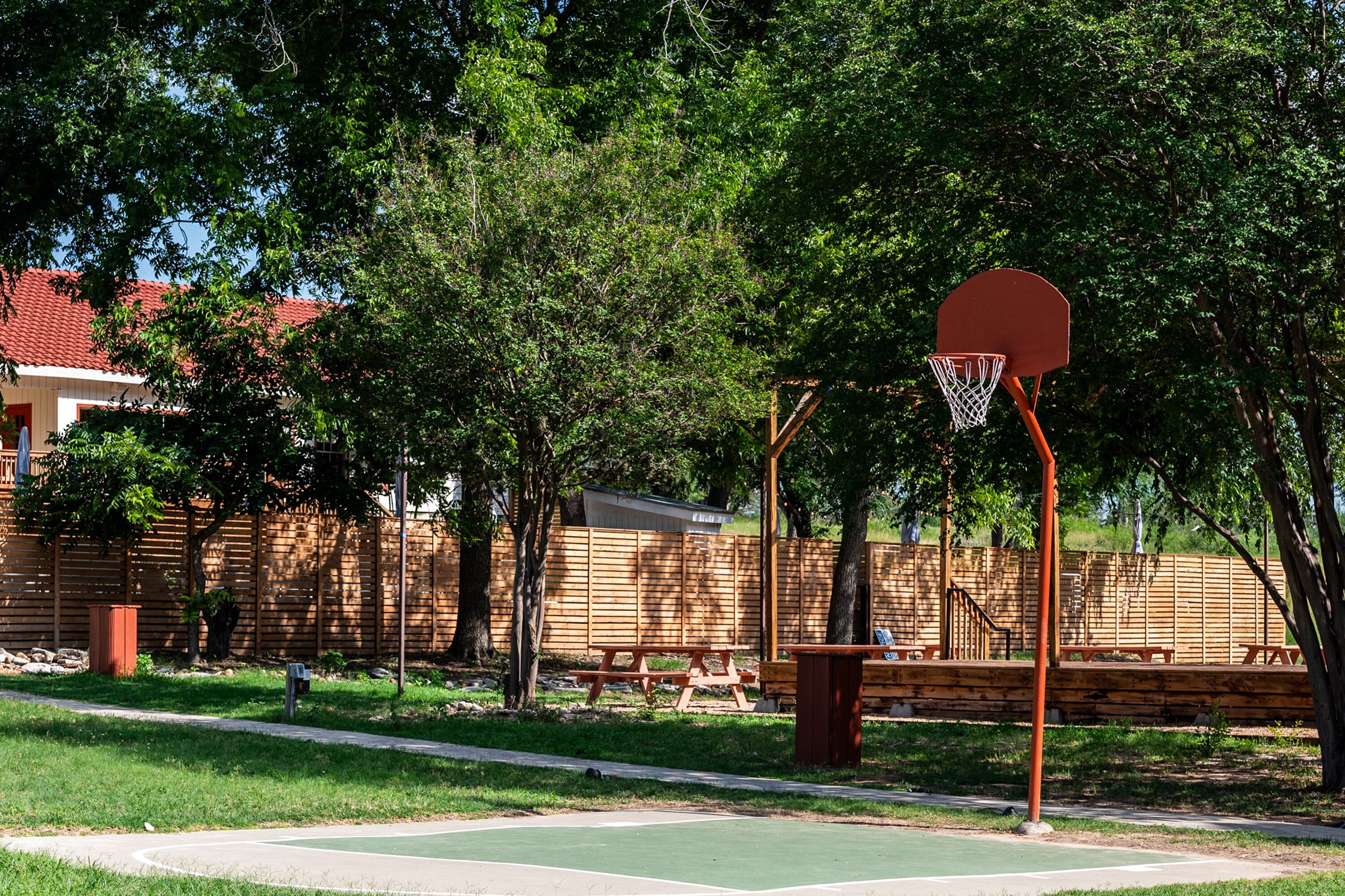 Ein Basketballplatz im Freien mit Holzzaun, Picknicktischen und Bäumen.