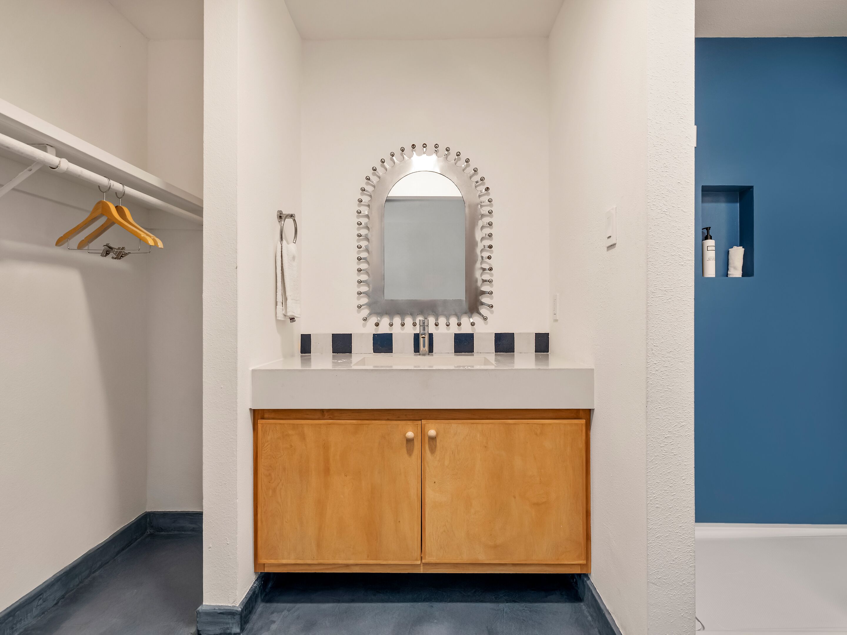 Een badkamer met een houten wastafelmeubel, een spiegel met decoratieve lijst, een handdoekhouder en een blauwe accentmuur.