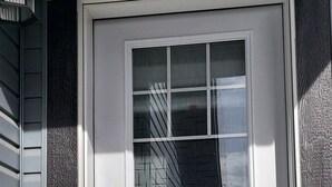 Una porta blanca amb un panell de vidre, un pom i un petit dispositiu electrònic a la part superior.