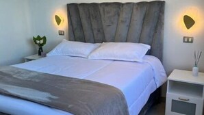 A modern bedroom with a large bed, two bedside tables, and wall-mounted lighting. - Home The Good | cana view (Punta Cana)