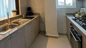 A narrow kitchen with a granite countertop, stainless steel sink, and a stove. - Home The Good | cana view (Punta Cana)