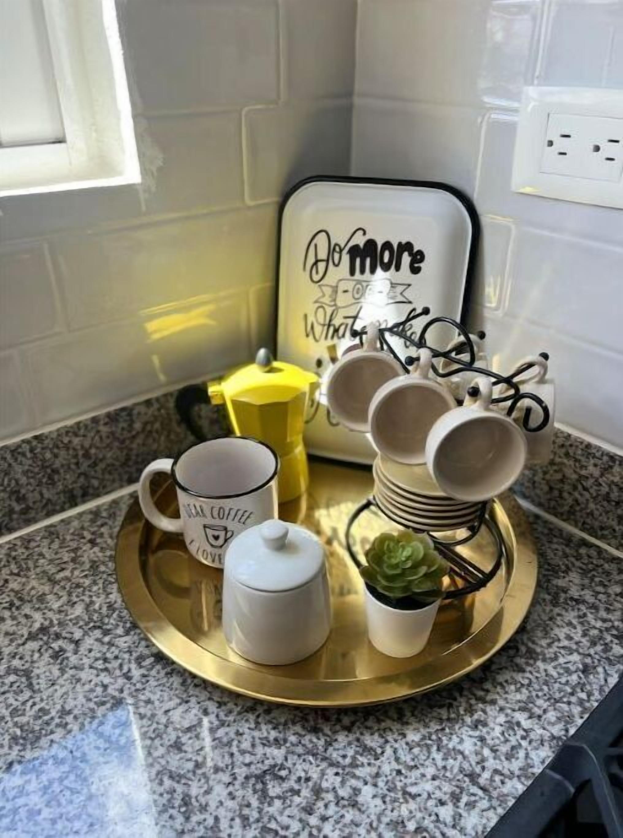 A kitchen counter with a coffee station, including a tray with a coffee pot, cups, and a small plant.