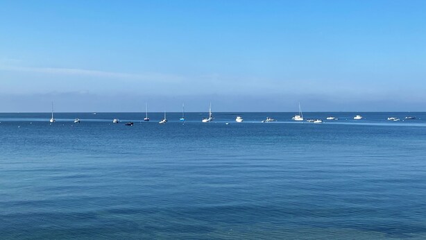 Une mer calme où l’on aperçoit plusieurs voiliers et yachts.