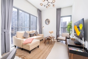 Een moderne woonkamer met een bank, fauteuil, televisie en grote ramen met uitzicht op de stad.