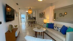 Una sala de estar moderna con un sofá, un sillón de mimbre, una mesita redonda y un televisor instalado en la pared.