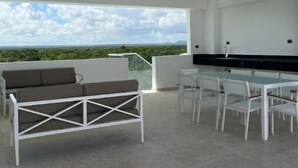 Un patio exterior con una mesa y sillas blancas, un sofá blanco y vistas al paisaje.