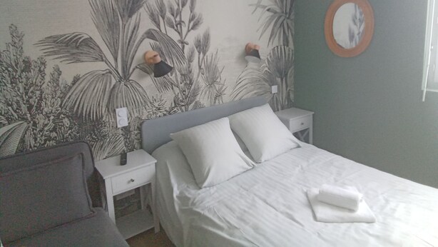A bedroom with a bed, two bedside tables, a nightstand, a chair, and a wall with a plant mural. - La renaissance (Condé-en-Normandie)