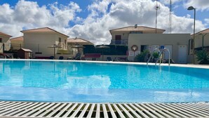 Ein Swimmingpool mit glatter, blauer Wasseroberfläche, umgeben von Gebäuden mit Ziegeldächern und einem wolkenlosen Himmel.