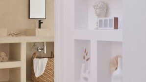 Ein modernes Badezimmer mit einem großen Spiegel, weißen Regalen mit Dekoration und einem Handtuchhalter.