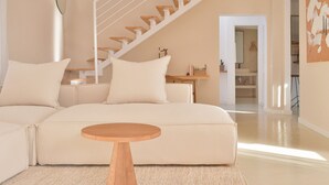 Ein modernes Wohnzimmer mit einem beigefarbenen Sofa, einem Holztisch und einer weißen Treppe.