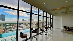 Une chambre d’hôtel moderne dotée de grandes fenêtres, offrant une vue sur la piscine, et comprenant un coin repas avec des chaises.