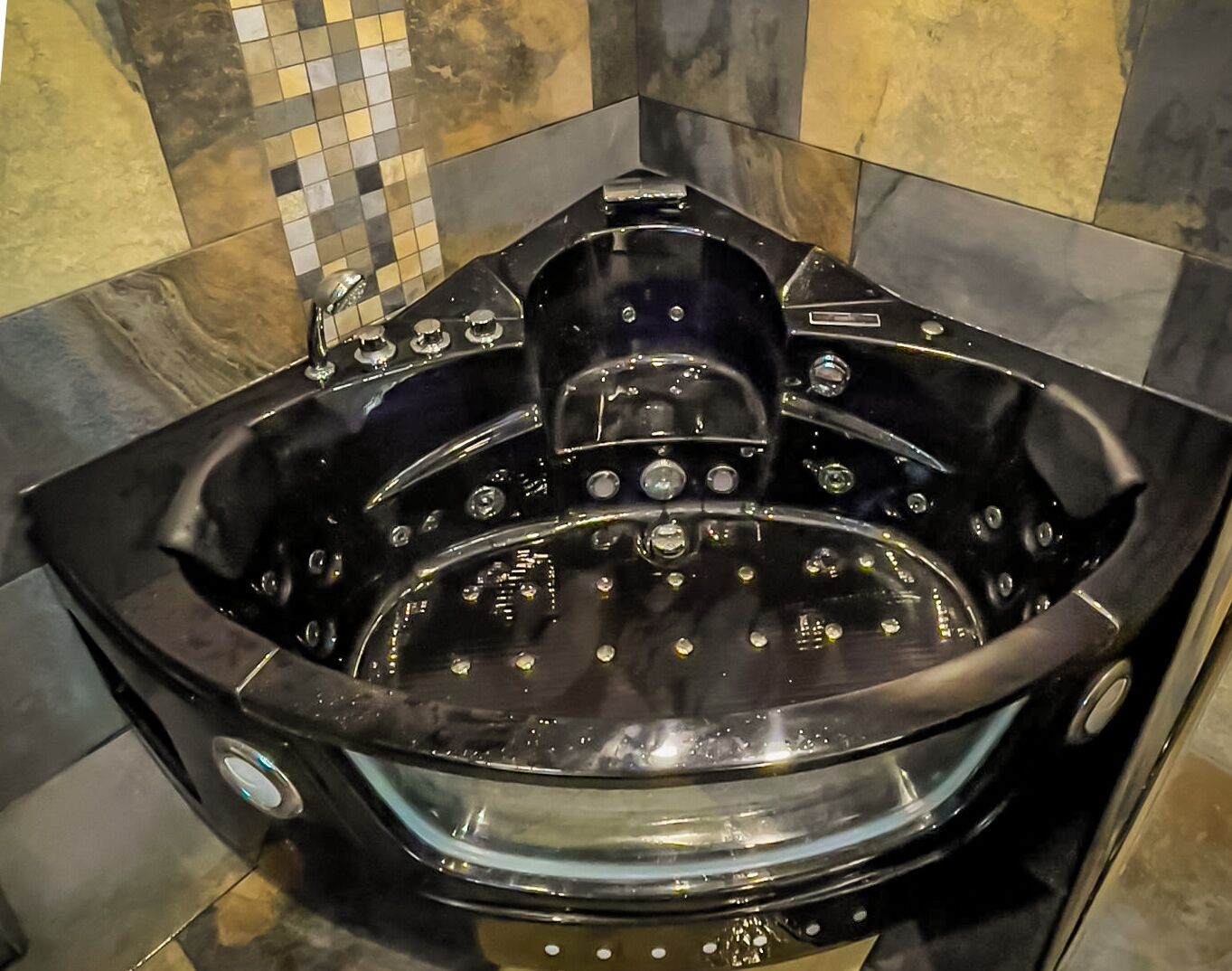 Un jacuzzi noir doté de plusieurs jets, installé devant un mur carrelé orné d’un motif en mosaïque.