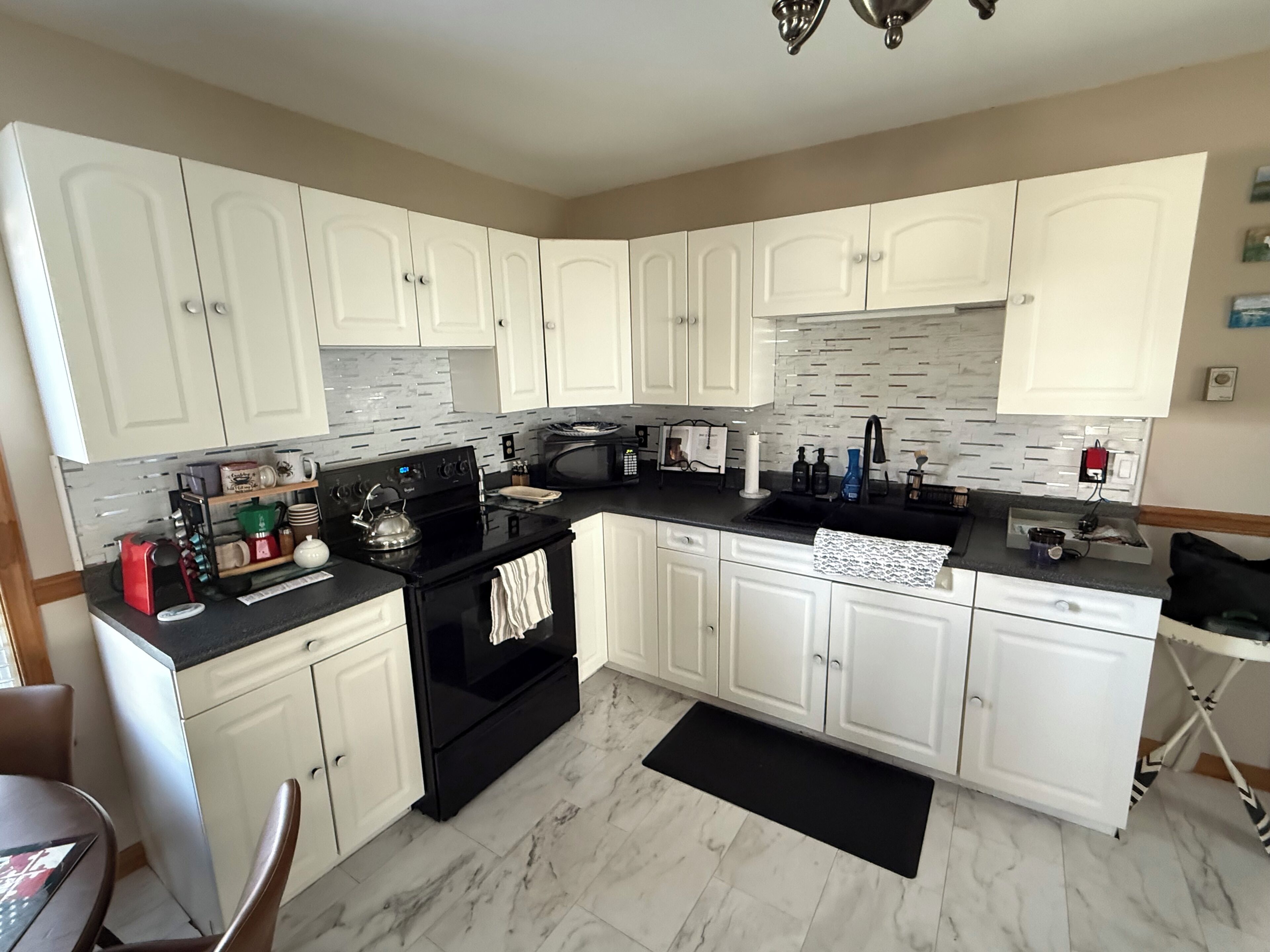 A kitchen with white cabinets, a black stove, a microwave, and a sink.