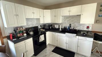 A kitchen with white cabinets, a black stove, a microwave, and a sink.