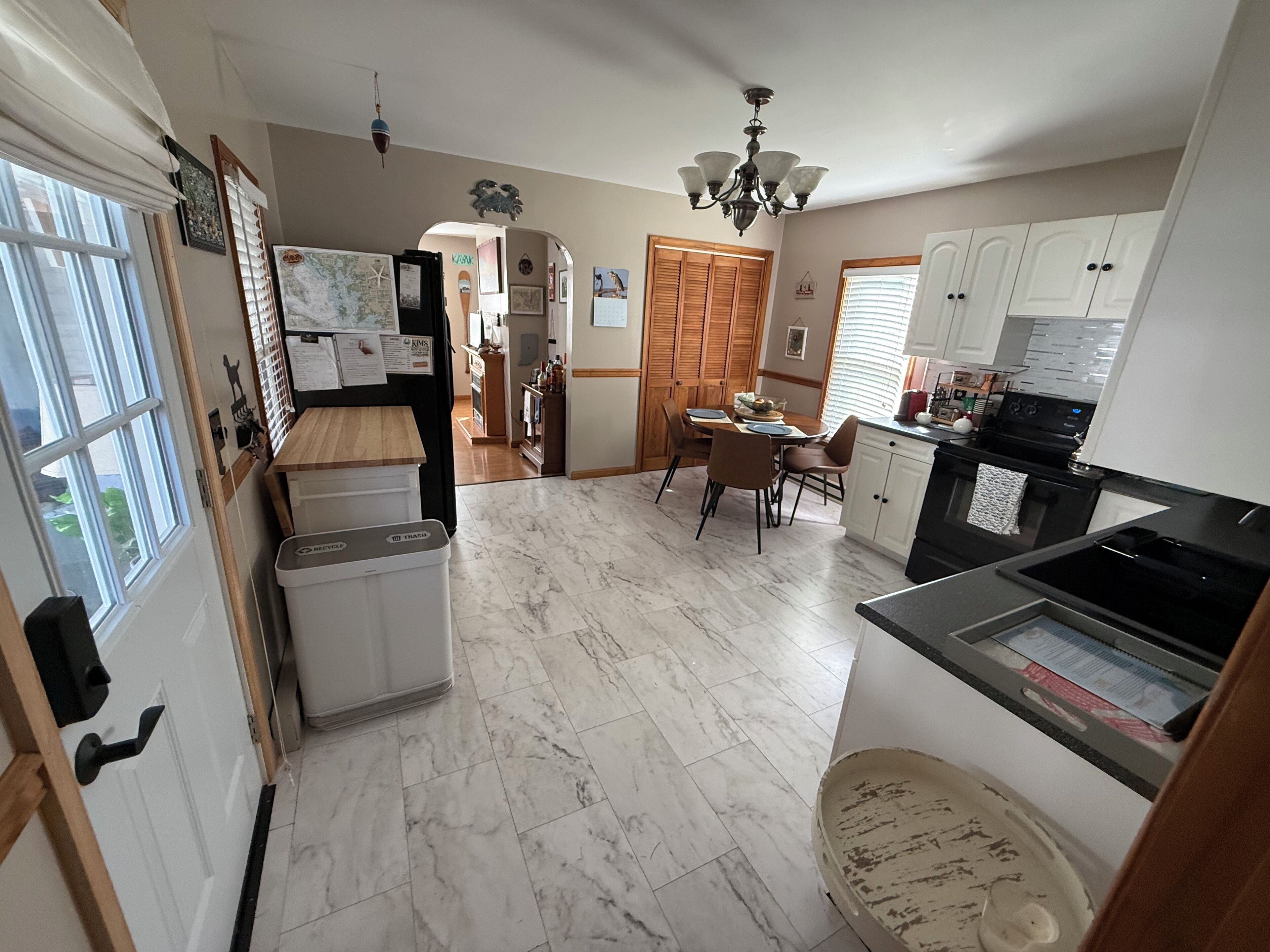 A kitchen with a dining area, a trash bin, and a refrigerator.