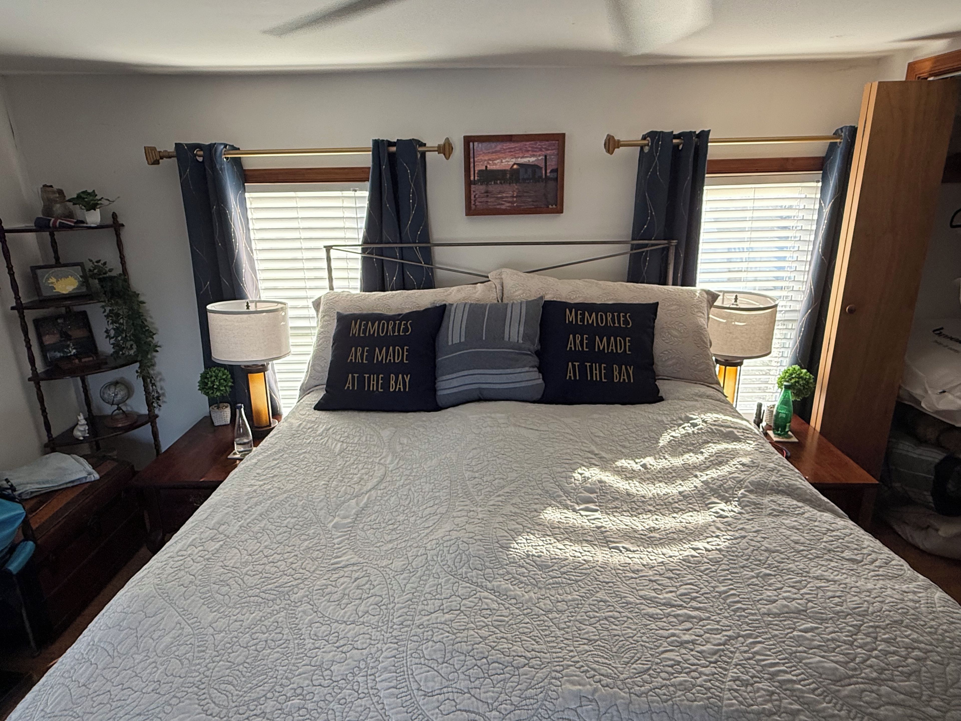 A bedroom with a bed, two bedside lamps, a nightstand, a shelf with decorative items, and a window with curtains.