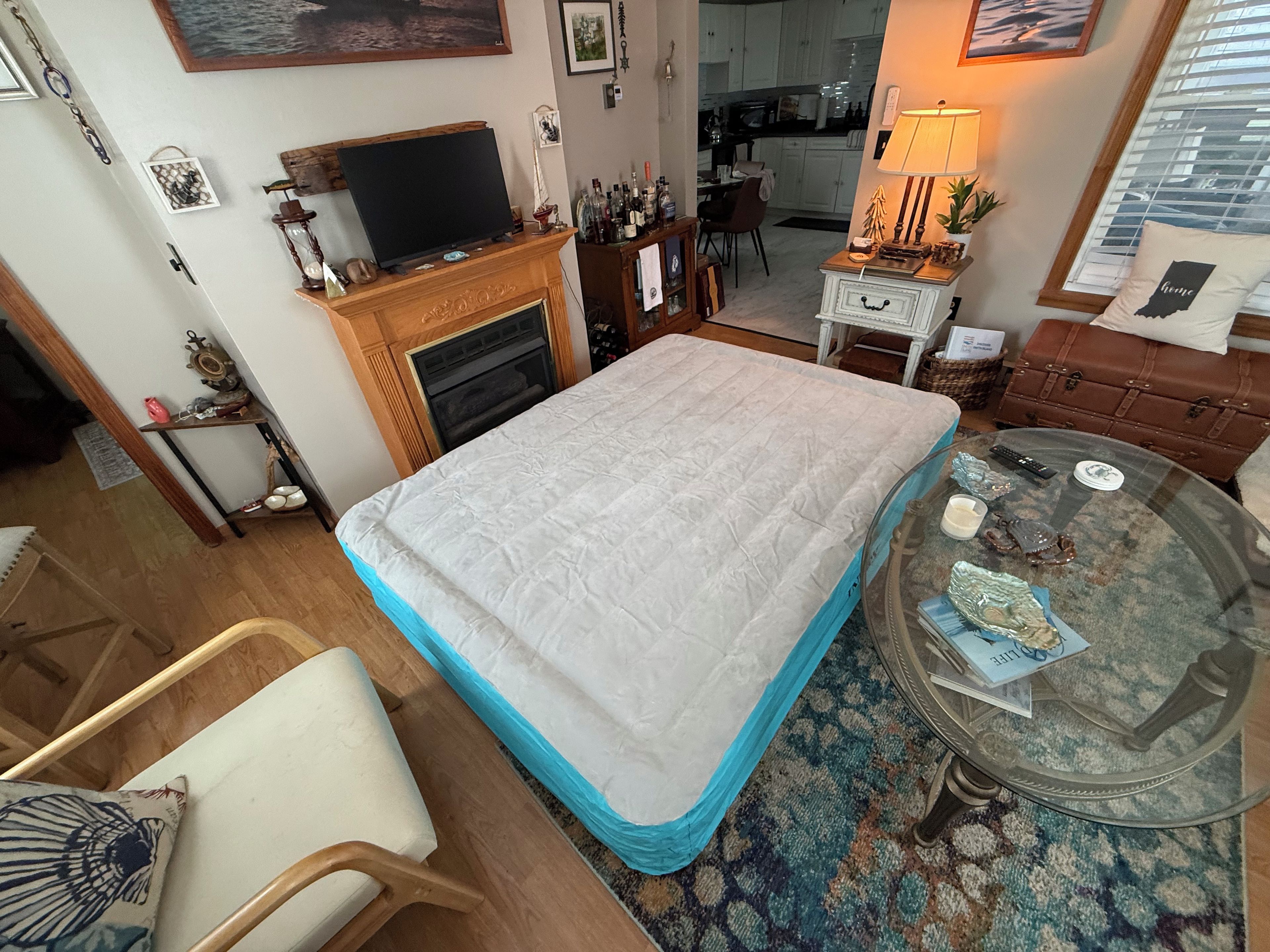 Una habitació amb un llit, una televisió sobre un suport, una llar de foc, una zona de menjador i una cuina al fons.