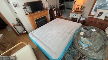 Una habitació amb un llit, una televisió sobre un suport, una llar de foc, una zona de menjador i una cuina al fons.