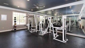 Un gimnasio con diversas máquinas de ejercicio, un espejo grande y una ventana con luz natural.