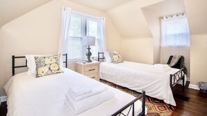 A bedroom with two beds, a nightstand, a lamp, and a window with curtains.