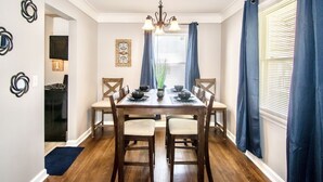 A dining room with a wooden table, four chairs, a chandelier, and blue curtains.