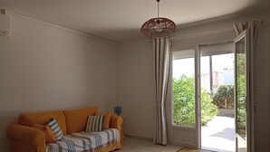 Een woonkamer met een bank, een hanglamp en een schuifpui die leidt naar een balkon.