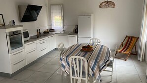 Een moderne keuken met witte kastjes, een eettafel met een geruit tafelkleed en een kleurrijke geruite stoel.
