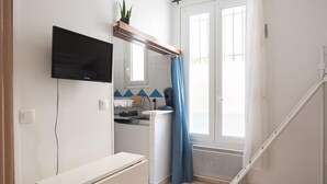 Une petite cuisine lumineuse, avec un plan de travail blanc, un four encastré et une fenêtre ornée de rideaux bleus.
