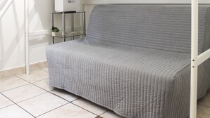 Un canapé gris avec un revêtement matelassé, un mur blanc et une étagère en verre sur laquelle repose un appareil électroménager blanc.