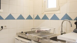 Une cuisine compacte avec des meubles blancs, un évier en acier inoxydable, un petit réfrigérateur et une fenêtre située au-dessus de l’évier.