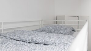 Un lit simple avec un cadre en métal blanc, une couvre-lit à motifs et un oreiller aux motifs similaires.