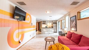 Ein modernes Hotelzimmer mit Küchenbereich, einem roten Sofa, einem kleinen Tisch und einem an der Wand befestigten Fernseher.