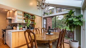 Una cocina moderna con comedor, sillas de madera, una araña y ventanas amplias.