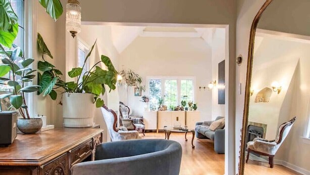 Un salón amplio con piso de madera, un espejo grande y un sillón azul.