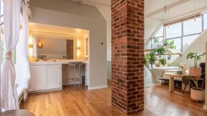 Una cocina moderna con armarios blancos, un pilar de ladrillo y un área de comedor con un sofá y plantas.