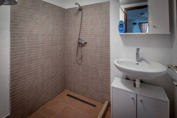 Une salle de bain avec une douche, un lavabo et un meuble de rangement.