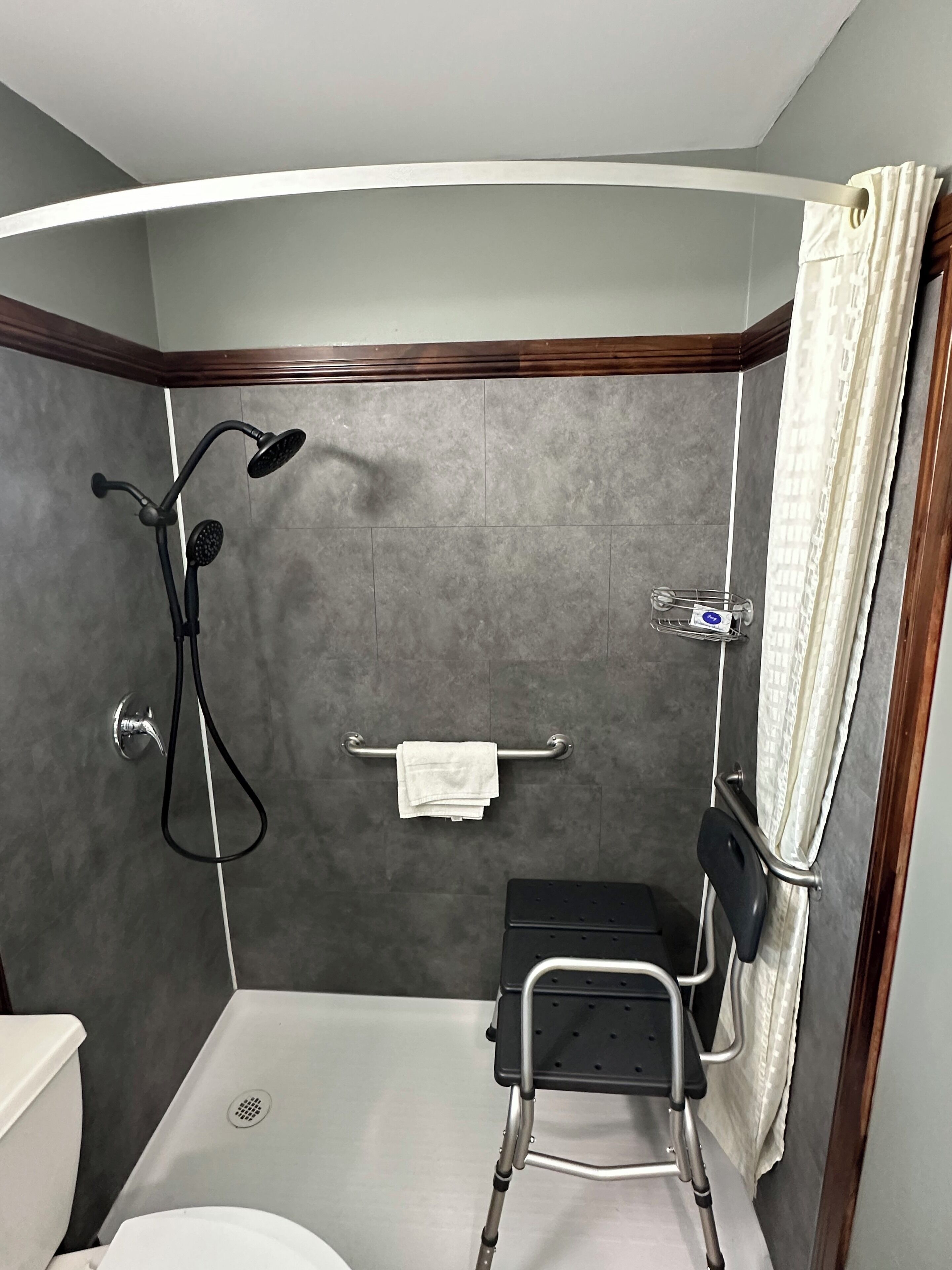 A small, modern bathroom with a shower, a toilet, and a wheelchair-accessible bench.